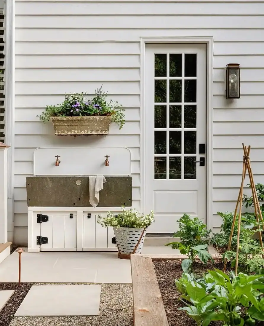 White horizontal boarded wall with an outdoor sink, copper taps and vegetable beds
