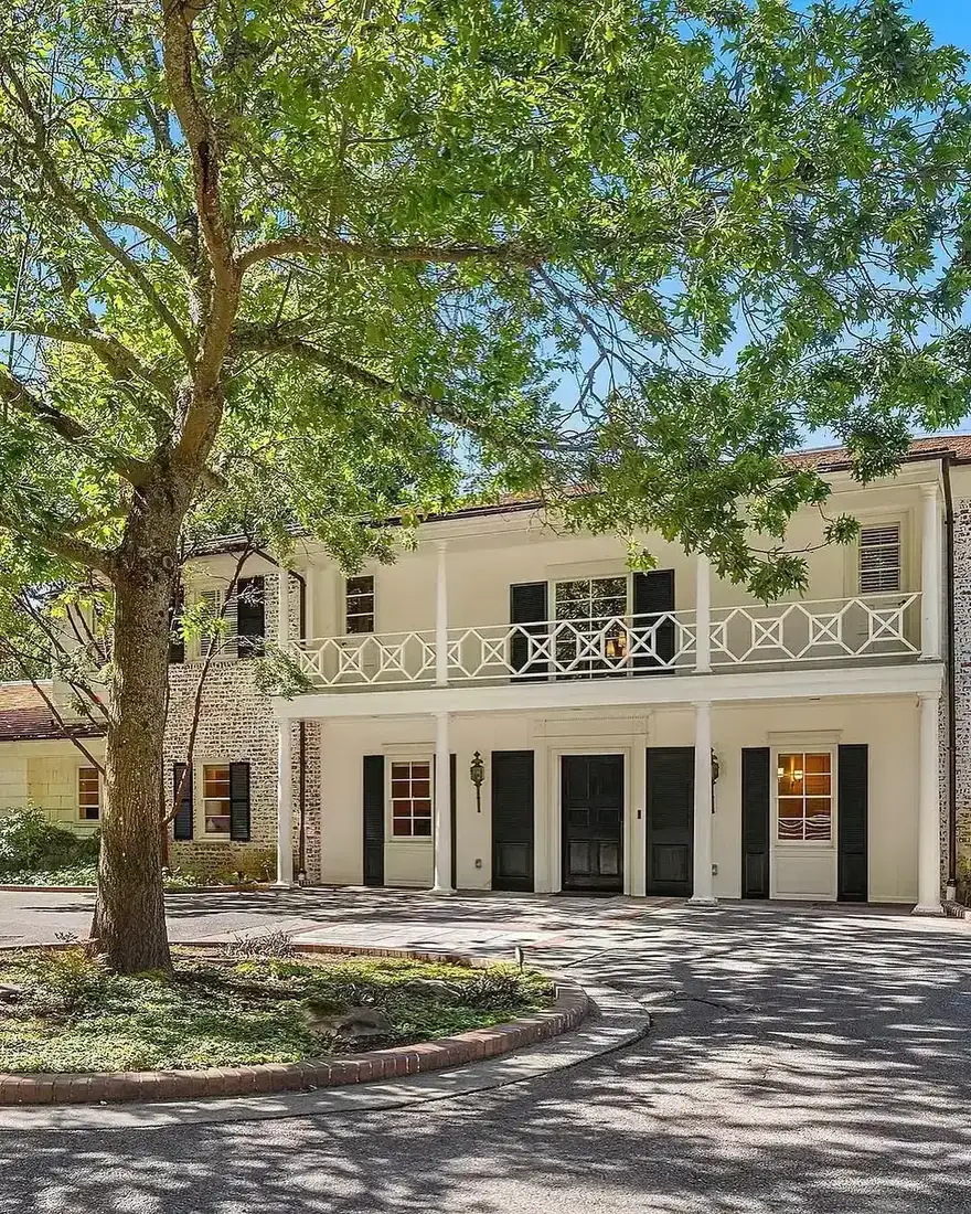 Cream brick house with black shutters and a white balcony above the doors
