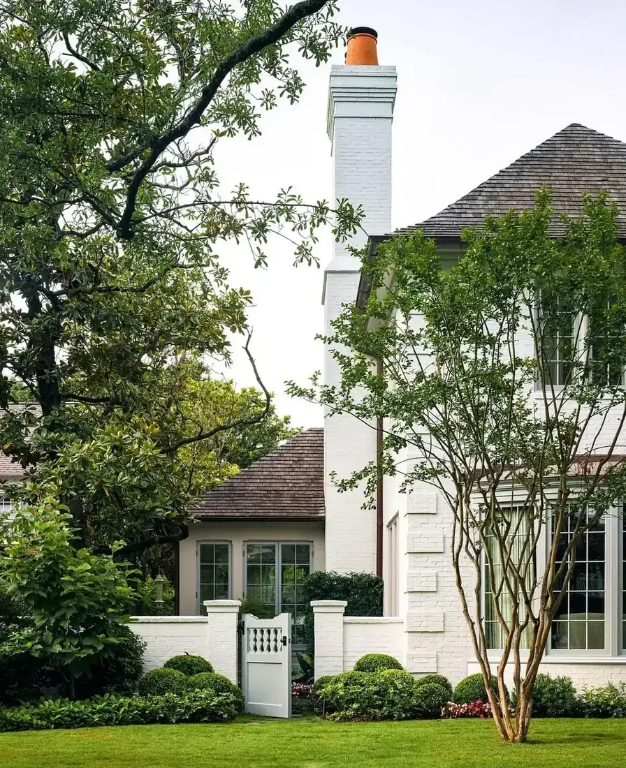 White painted brick chimney and garden wall with a gate and lawn
