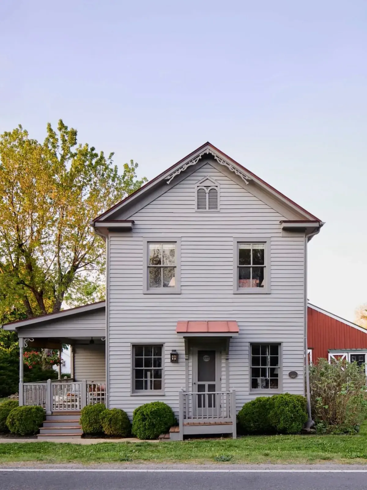 Grey farmhouse beside a red barn with a copper awning