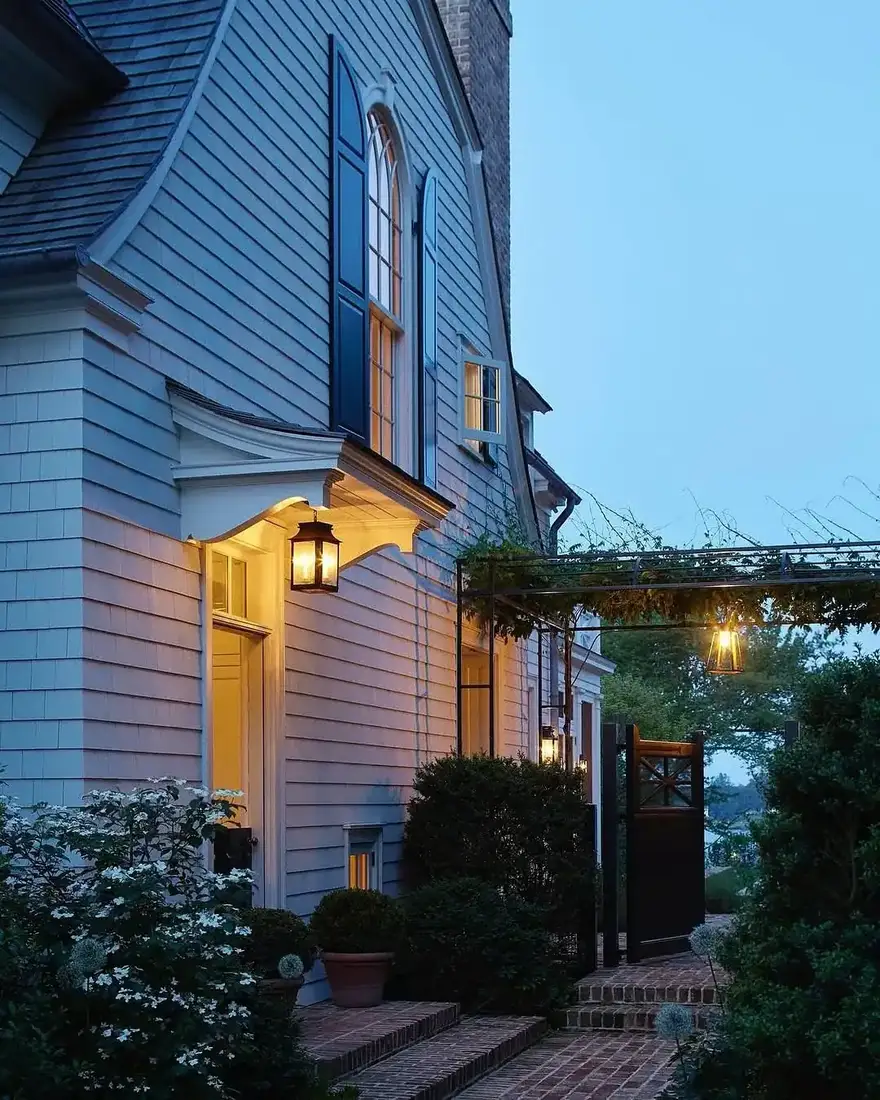 Blue shingle house at dusk with warm lantern light over the porch