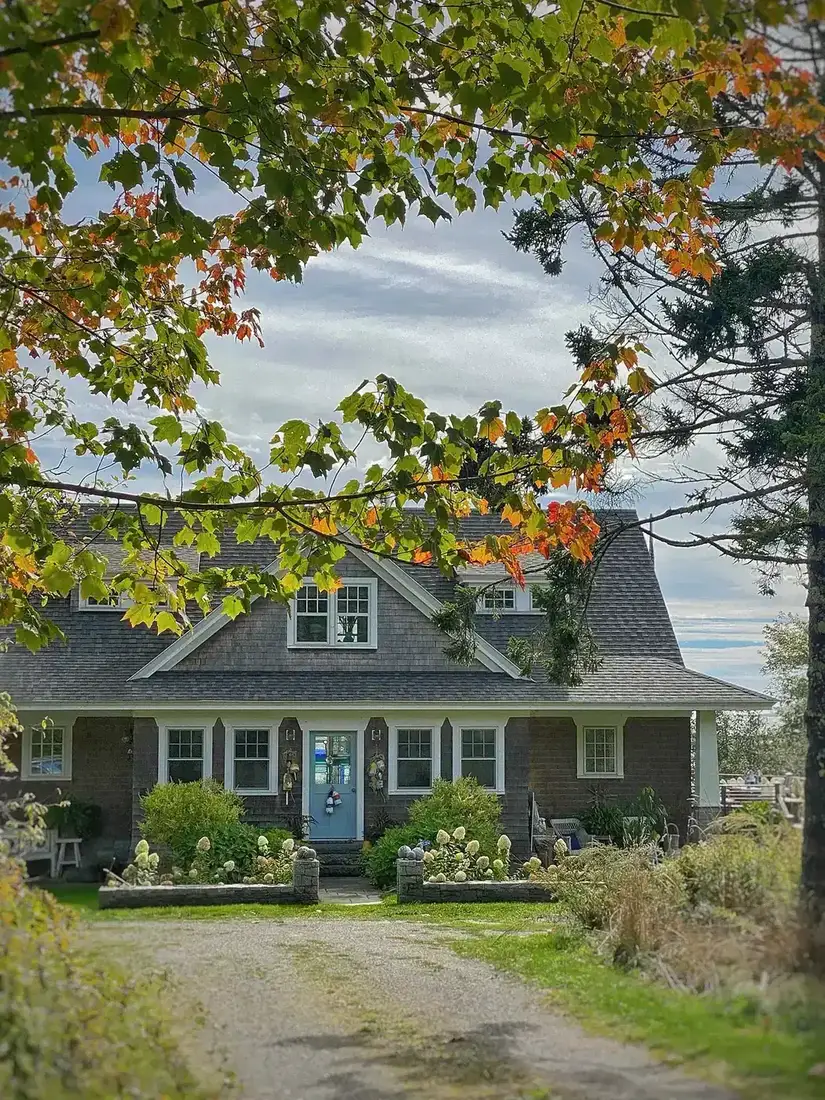 Dutch colonial house in brown shingles with gravel drive