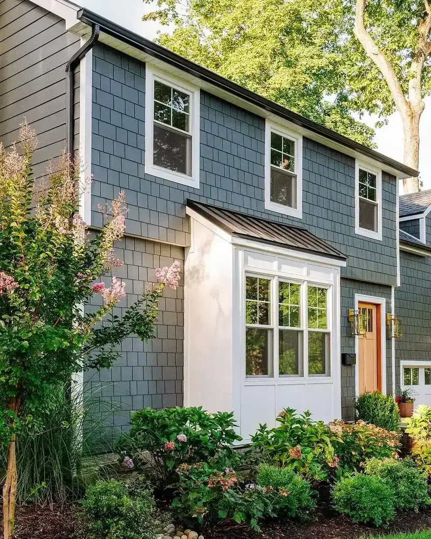 Blue grey stained shingle house with white bay window and planting