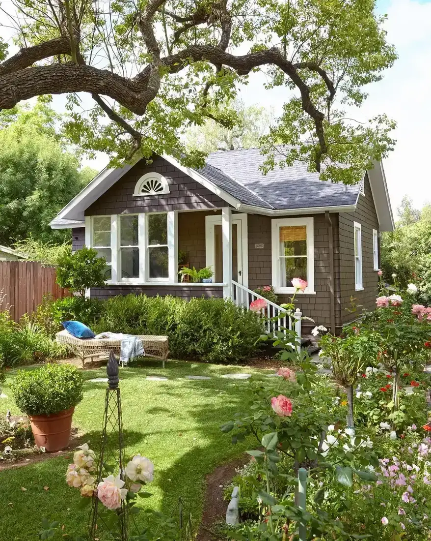 Brown shingle bungalow with white porch and roses in front