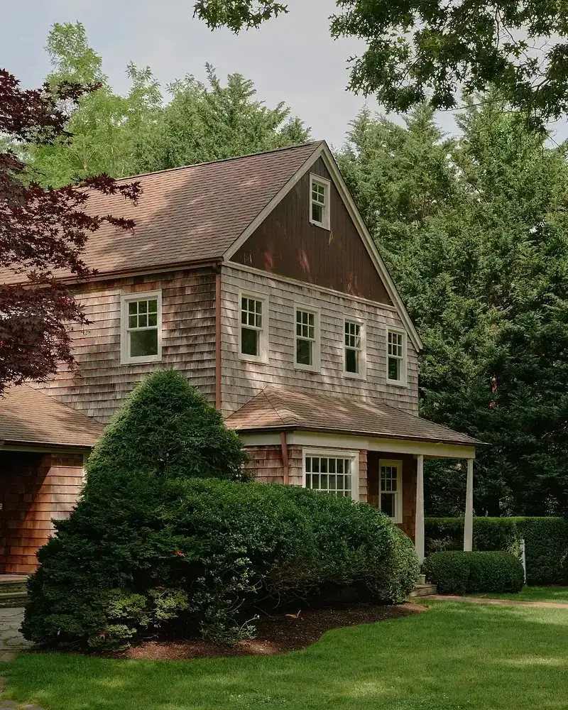 Brown shingle walls weathering unevenly with white windows above a green lawn