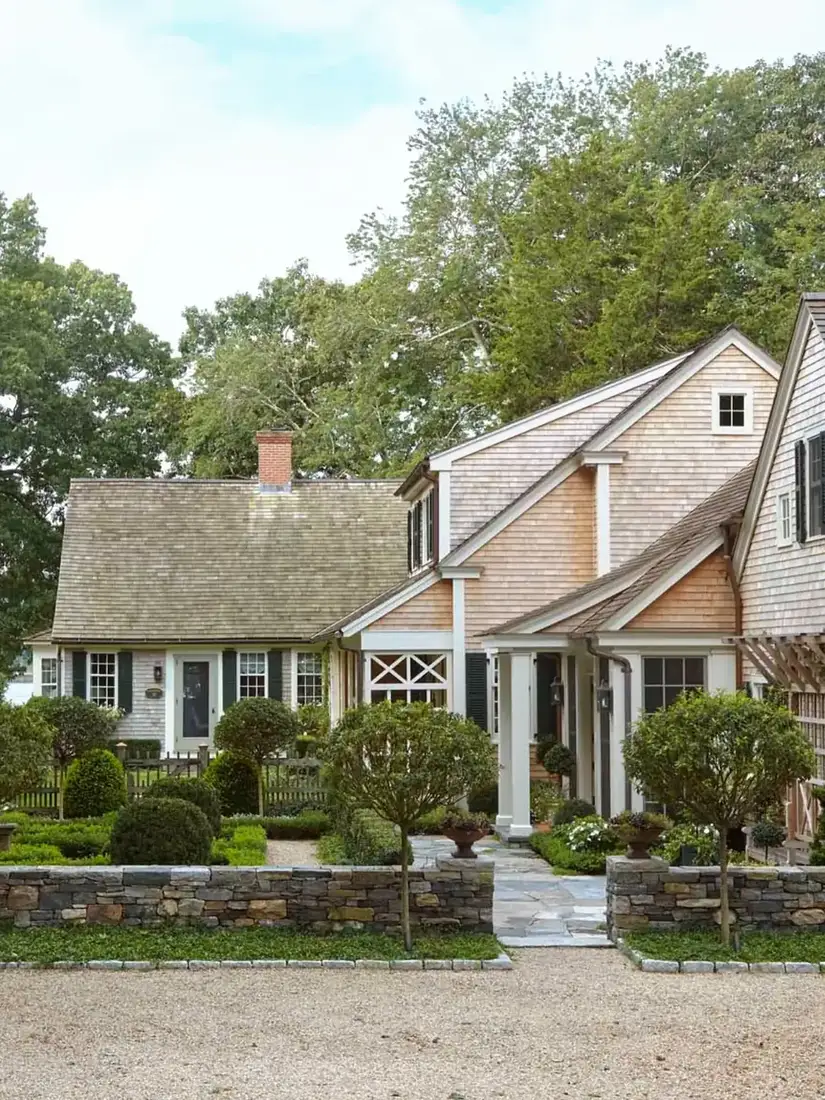 Pale honey shingle cape with stone wall and clipped topiary