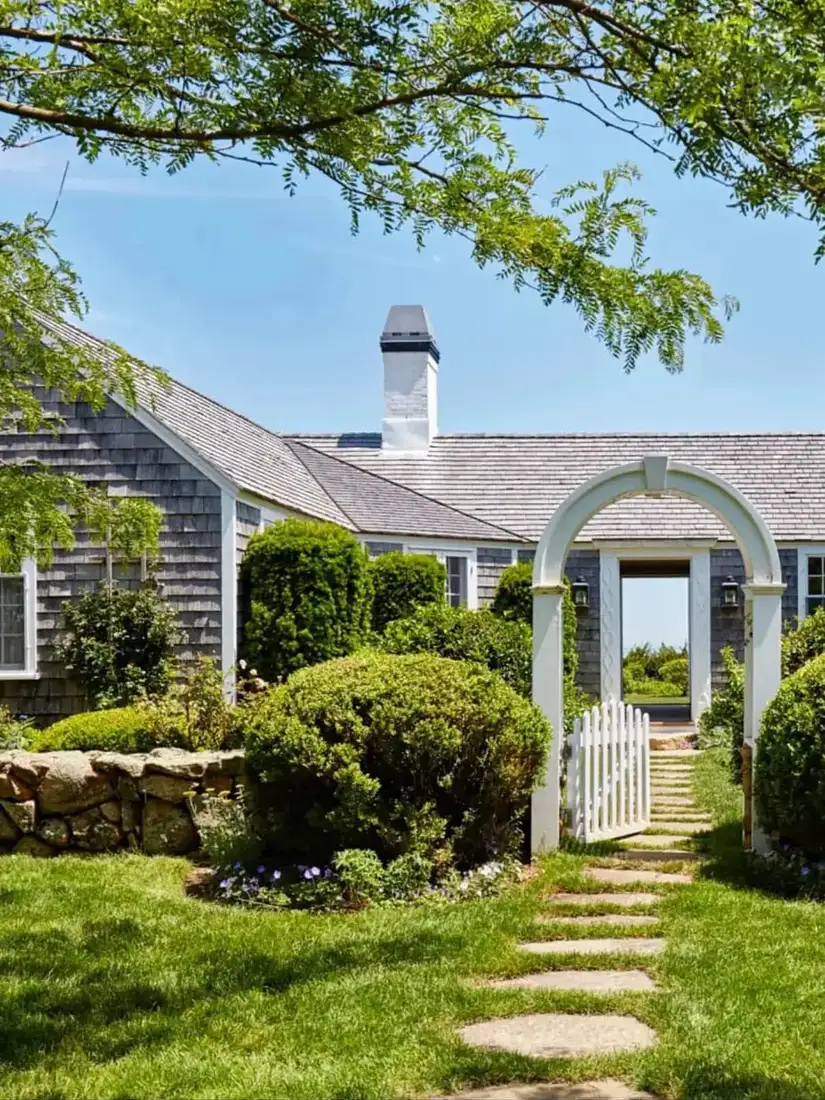 Silver grey shingle cottage with white arbor gate and stone wall