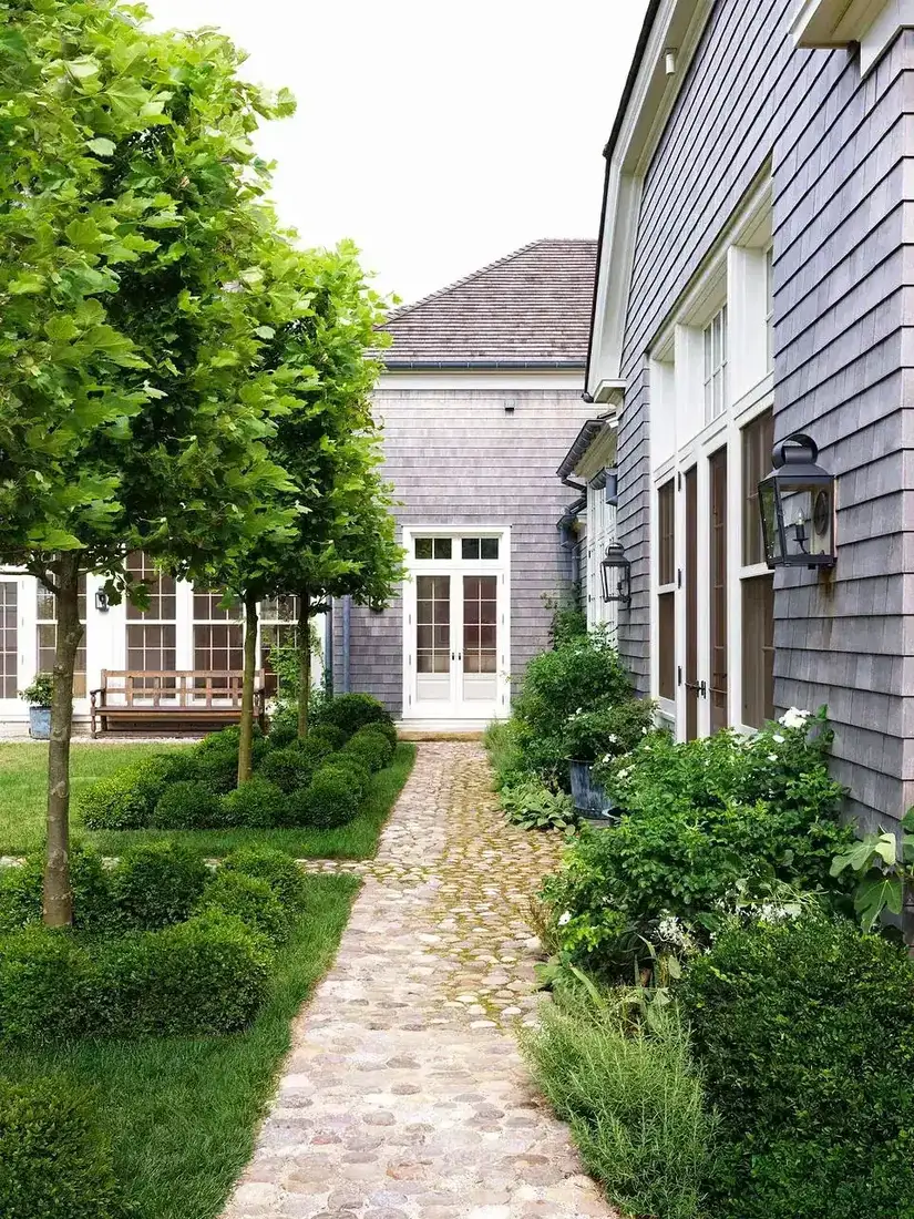 Silvered shingle side wall beside a cobbled path with pleached trees
