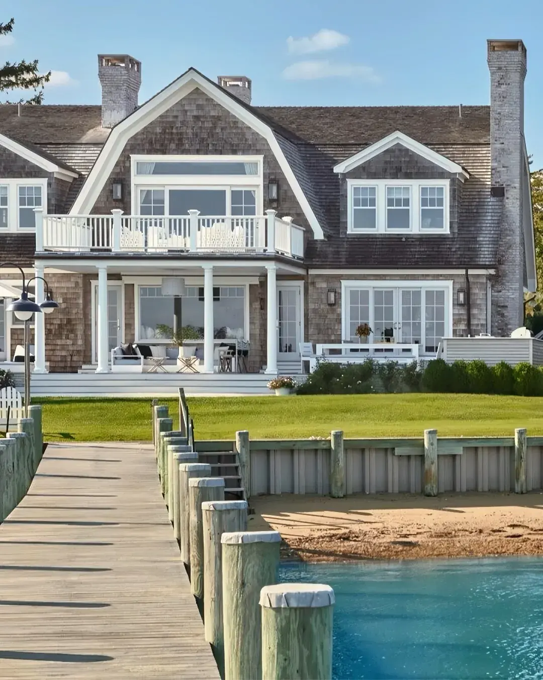 Shingle style waterfront house seen from the water with a dock and pilings in front