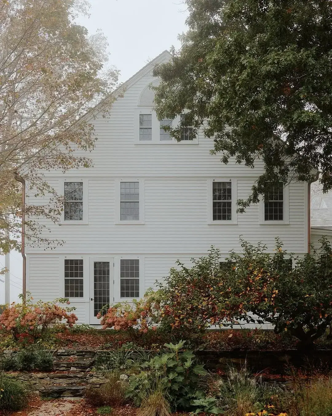 White clapboard gable with a shingle roof and garden beds below