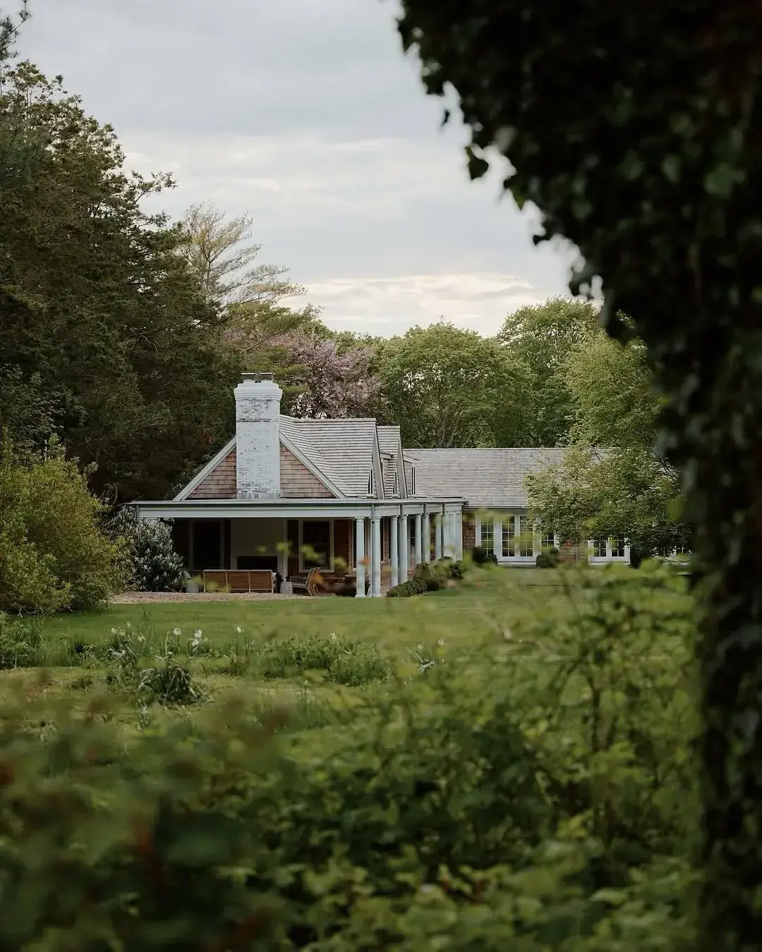 White shingle cottage with a chimney standing in a meadow garden