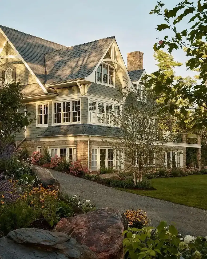 Shingle Style house with a stone base and shingle wrapping the curved roof of a bay
