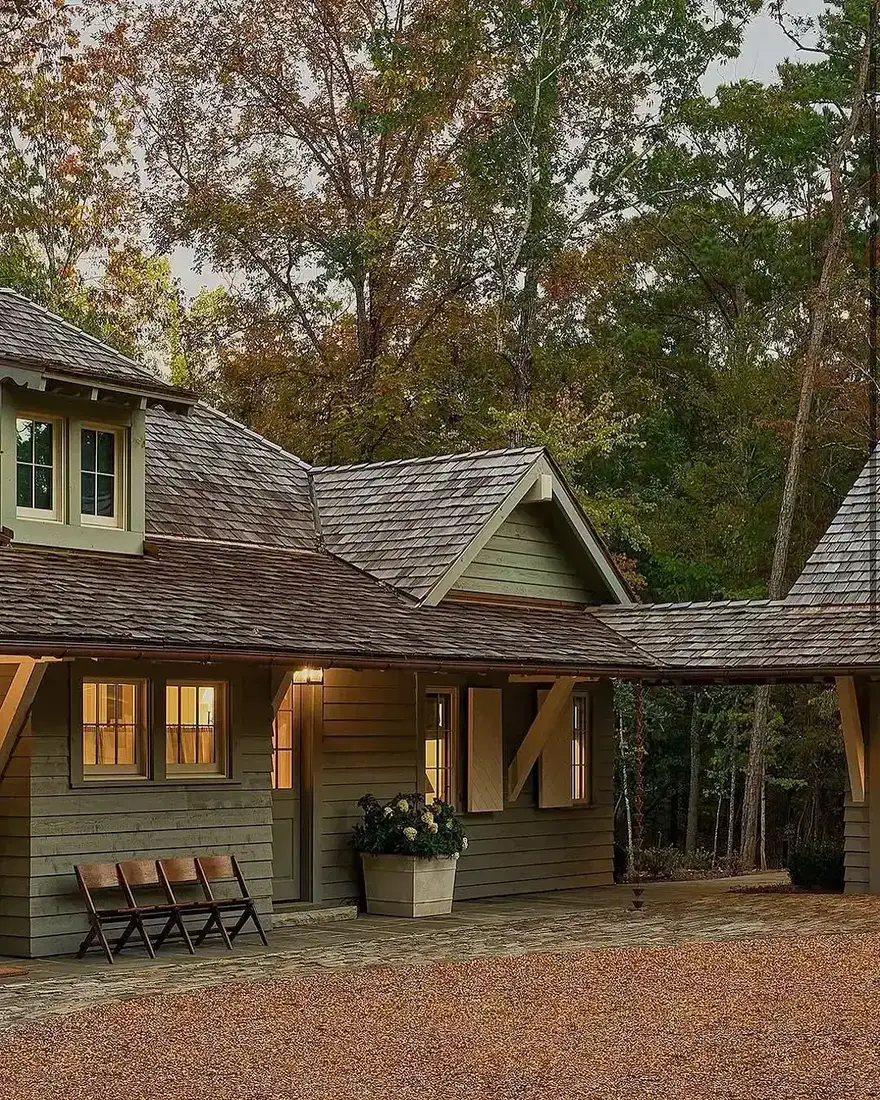 Sage green cottage with horizontal boarding, shingle roofs, breezeway to carport, stone paving, gravel court, three folding chairs and a planter