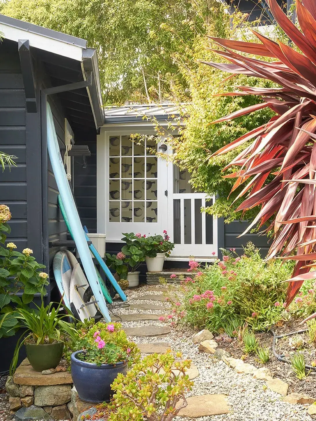 Charcoal painted timber cottage with crisp white door, surfboards, gravel and stone path