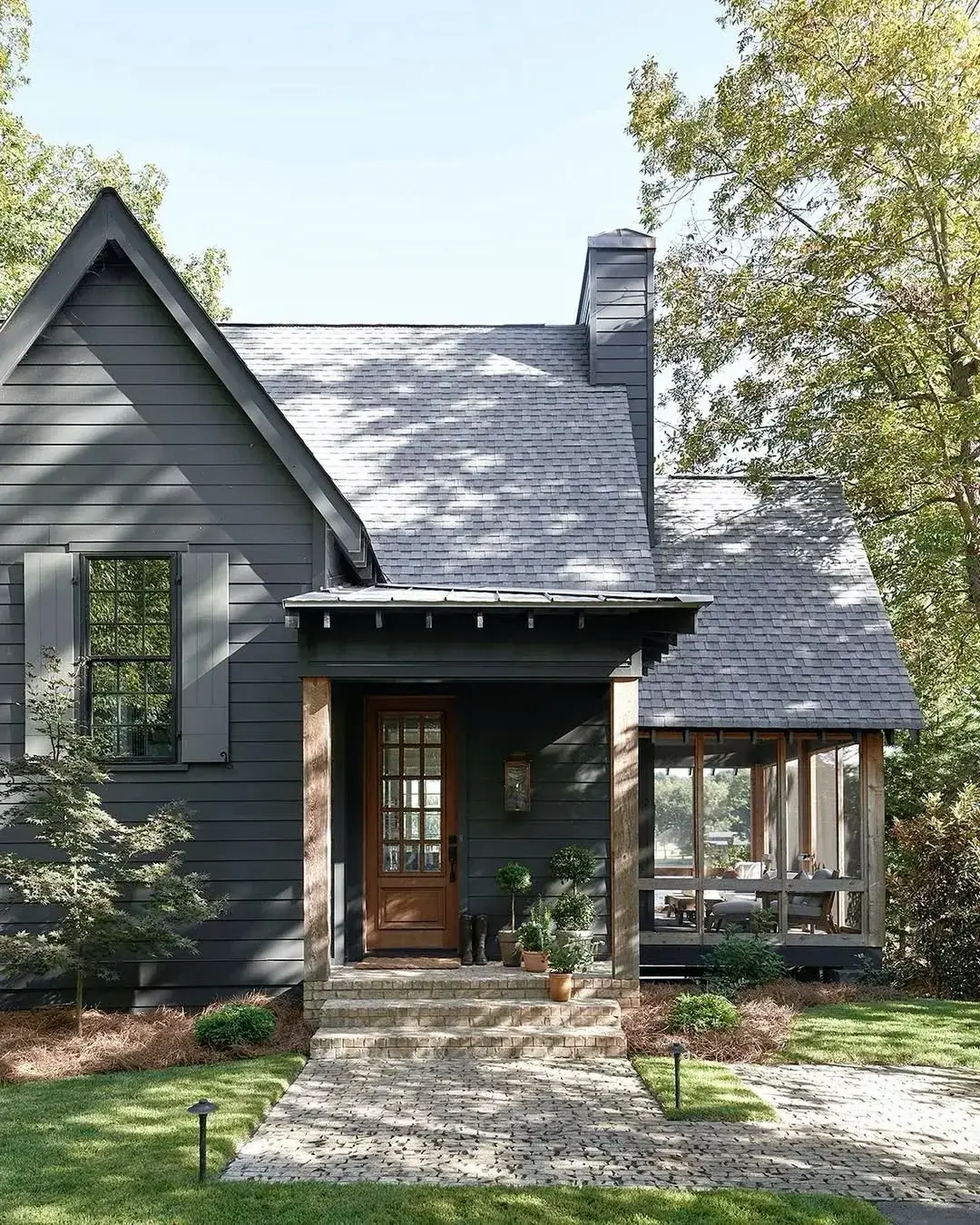 Dark grey boarded cottage with steep gable, timber porch posts and a glazed wooden door