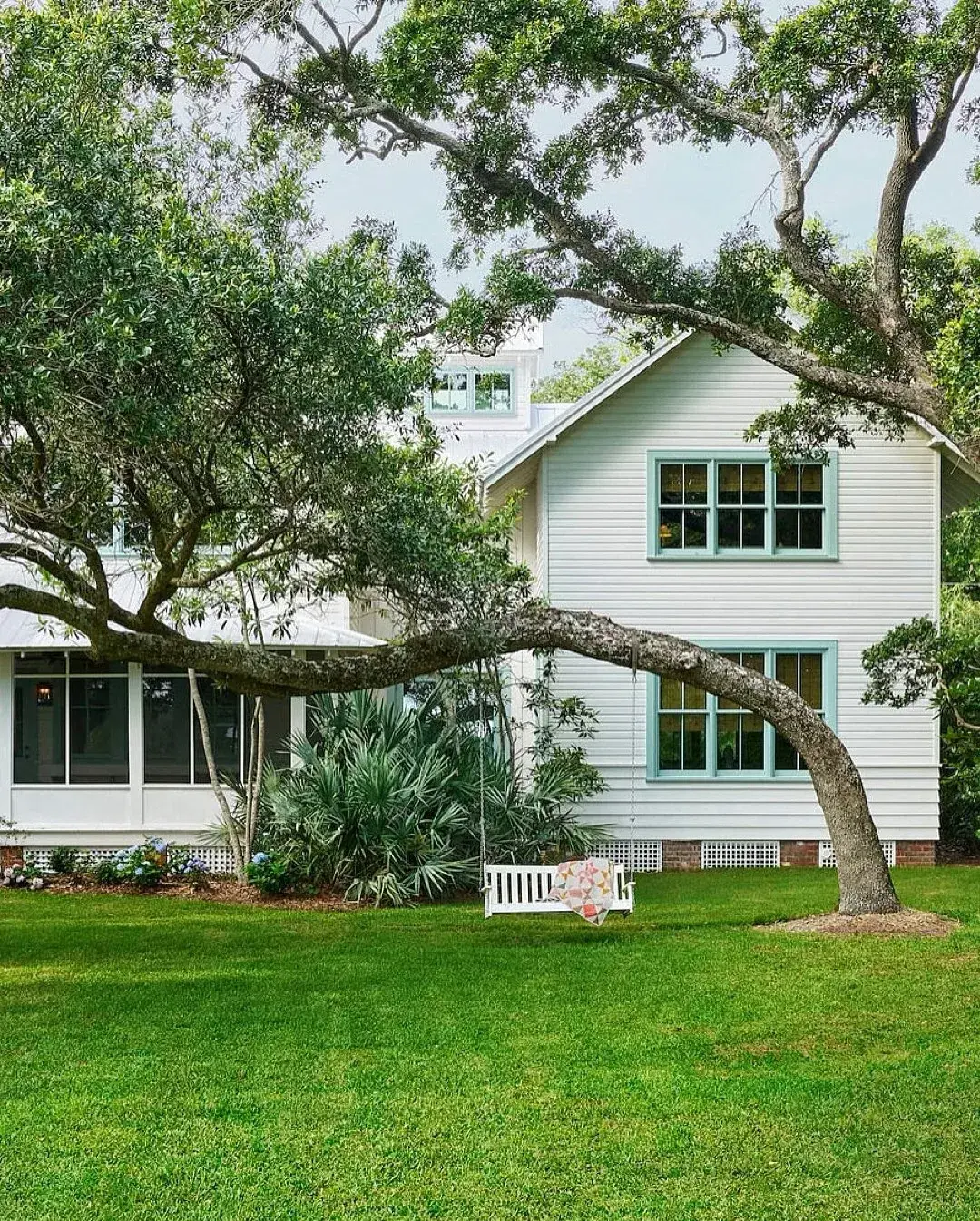 White weatherboard cottage with aqua trim and a bench swing hung from a leaning oak limb