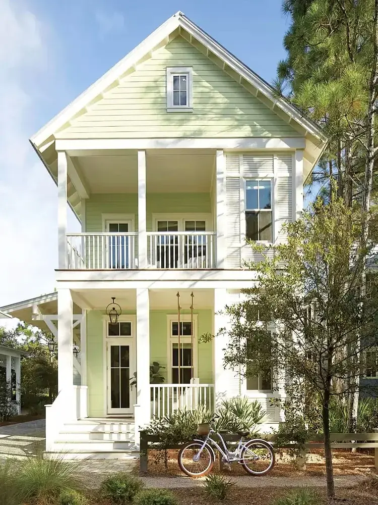 Tall pale green cottage with a double height porch, white columns and a bicycle by the steps