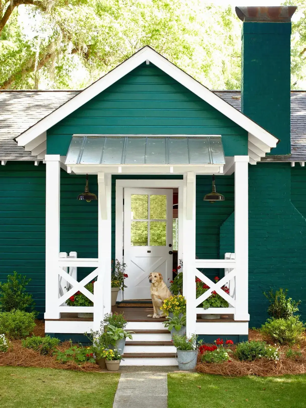 Deep teal cottage with a white gabled porch, cross braced rails and a dog on the steps