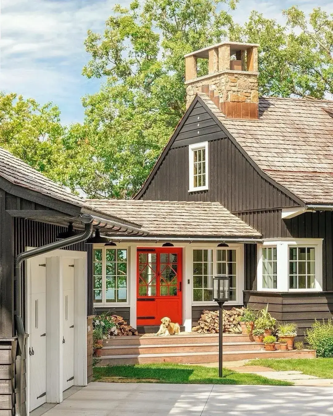 Near-black stained cottage under a natural cedar shake roof, with a red front door