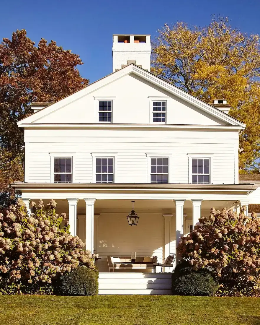 White farmhouse with matching white trim and columns, contrasted only by dark window sash