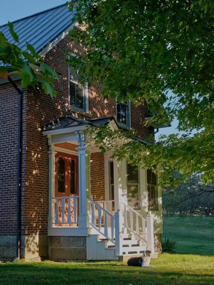 Dark brick farmhouse with white porch steps and white columns