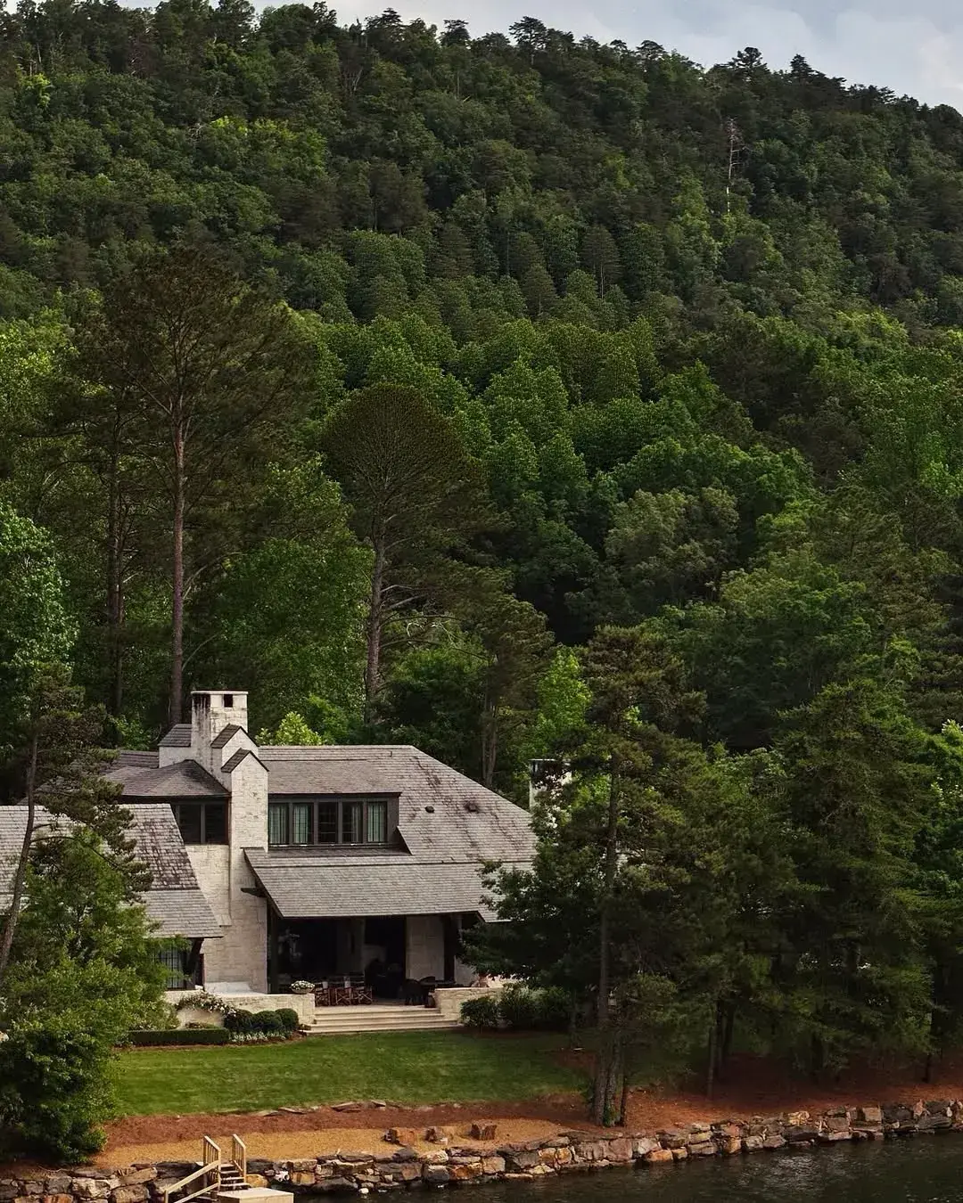 White lake house set on a forested mountain hillside above water