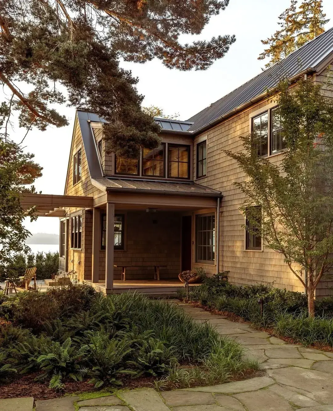Weathered cedar shingle house with a dark charcoal standing seam roof and a timber porch
