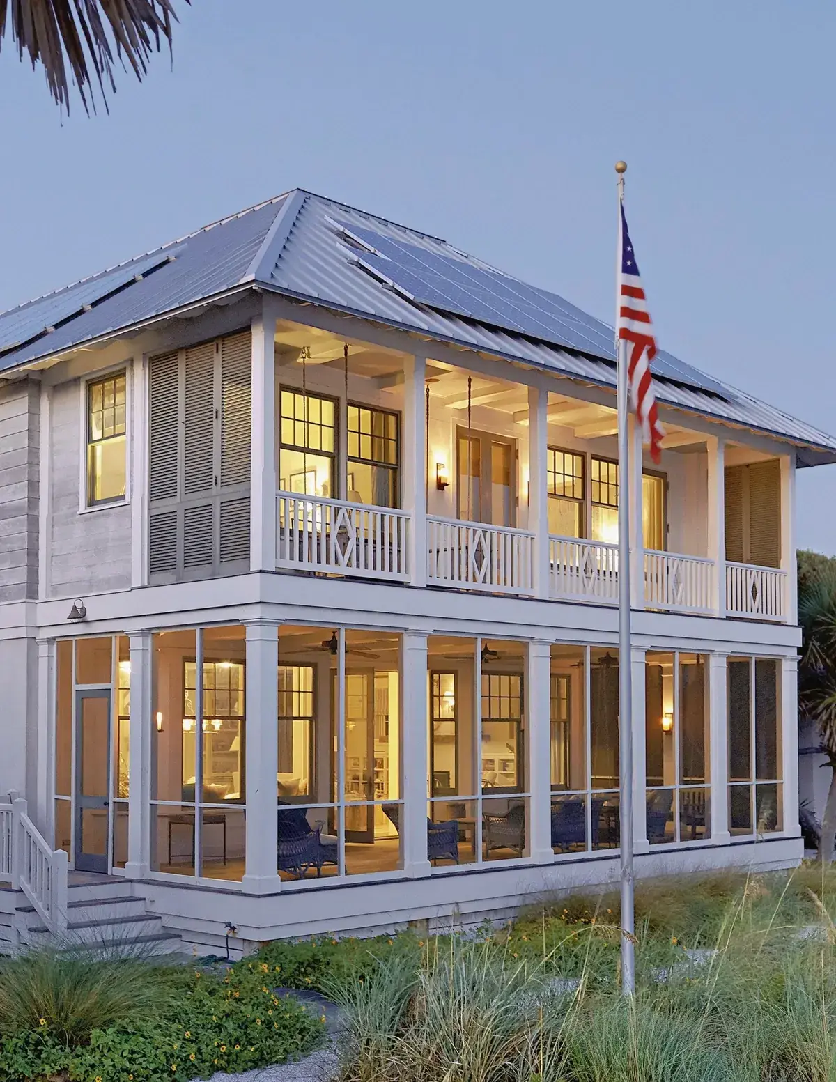 White coastal house with a bright silver standing seam roof carrying solar panels above a screened porch