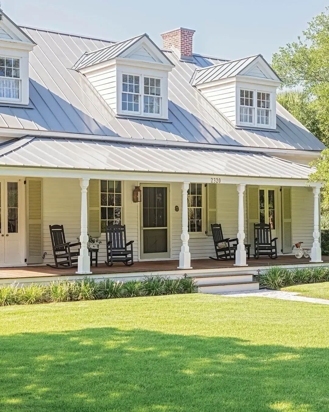 Cream cottage with a pale silver metal roof, three dormers and a porch with rocking chairs