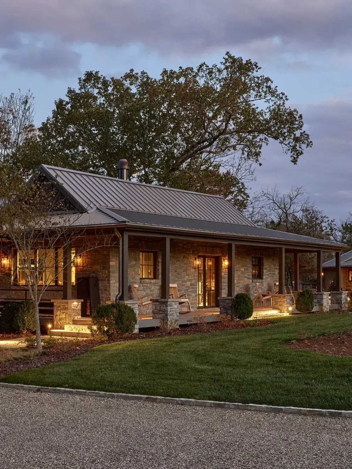Stone ranch with a dark metal roof and a deep porch lit warm at dusk
