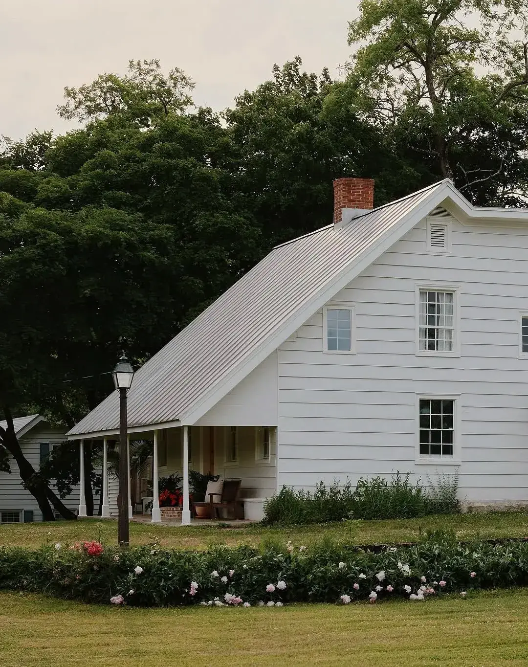 White barn form house with a long pale metal roof reaching to a columned porch