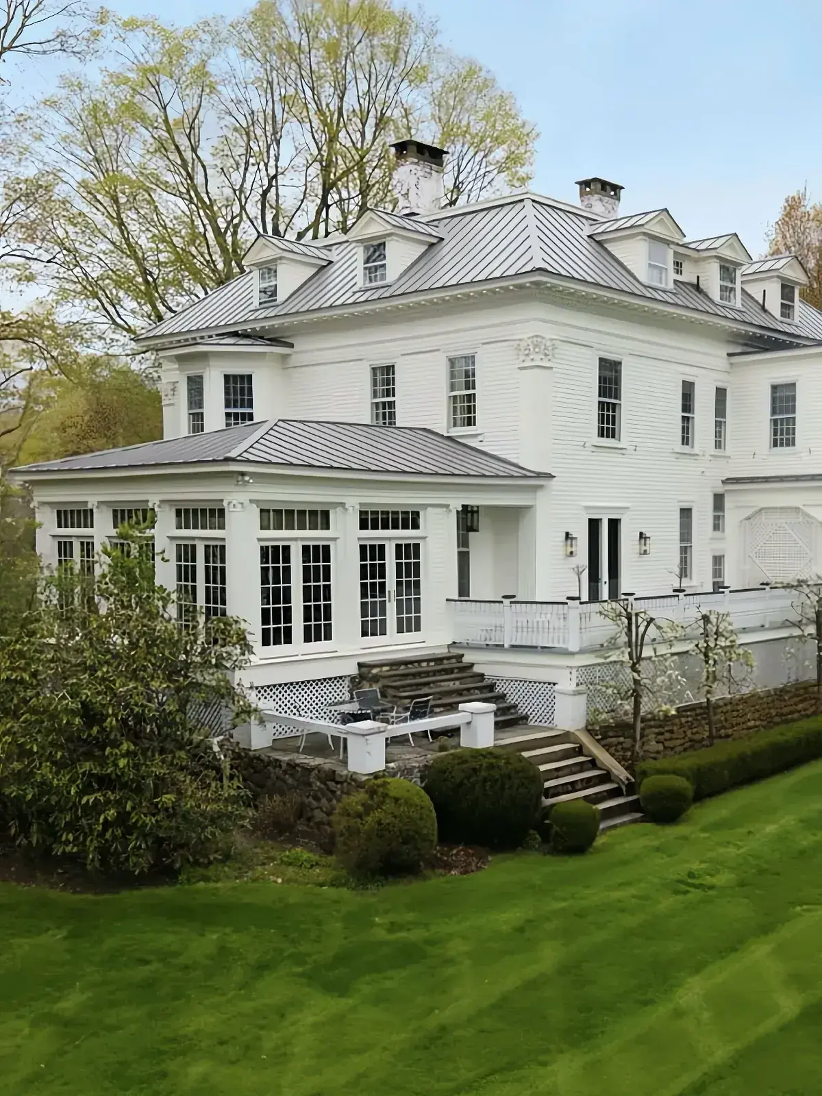 Large white clapboard house with a complex pale silver standing seam roof over a conservatory and dormers