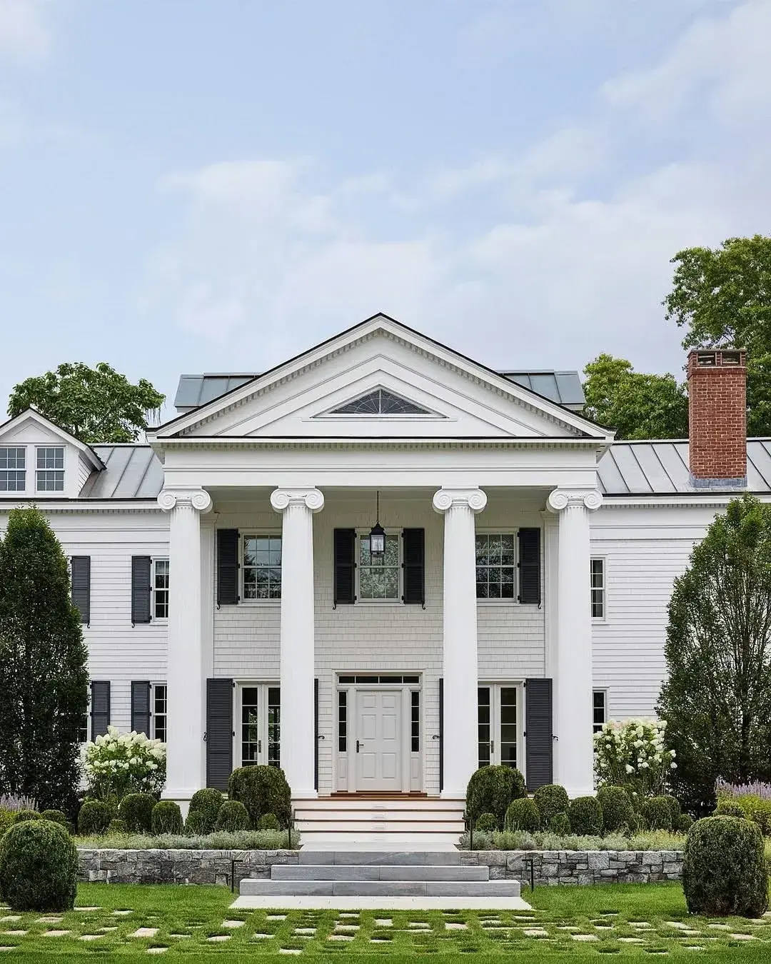 White Greek revival house with four columns, dark shutters and pale silver metal wings