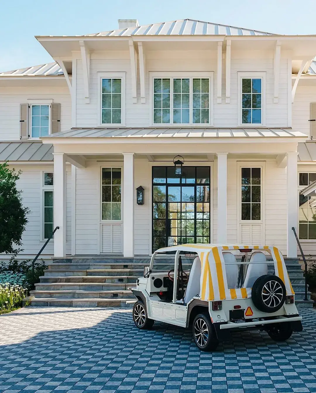 White lowcountry house with a pale silver double roof, central glass doors and a yellow striped beach buggy