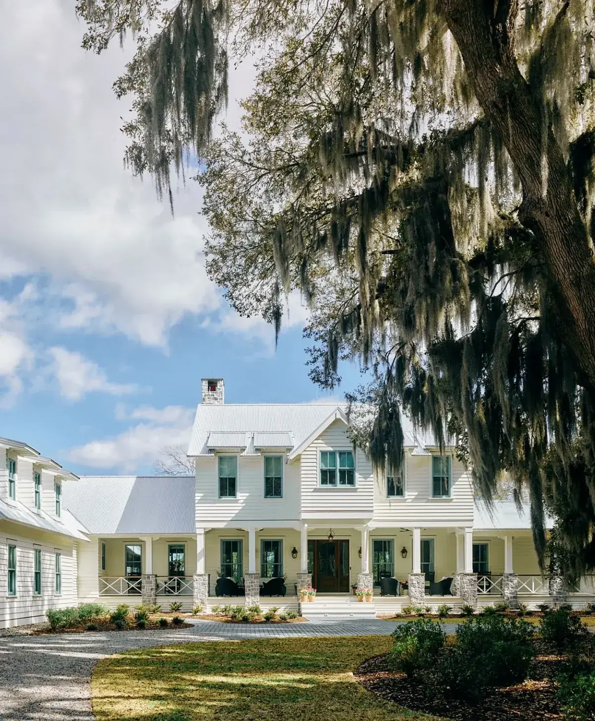 White farmhouse with a very pale metal roof under live oaks draped with Spanish moss