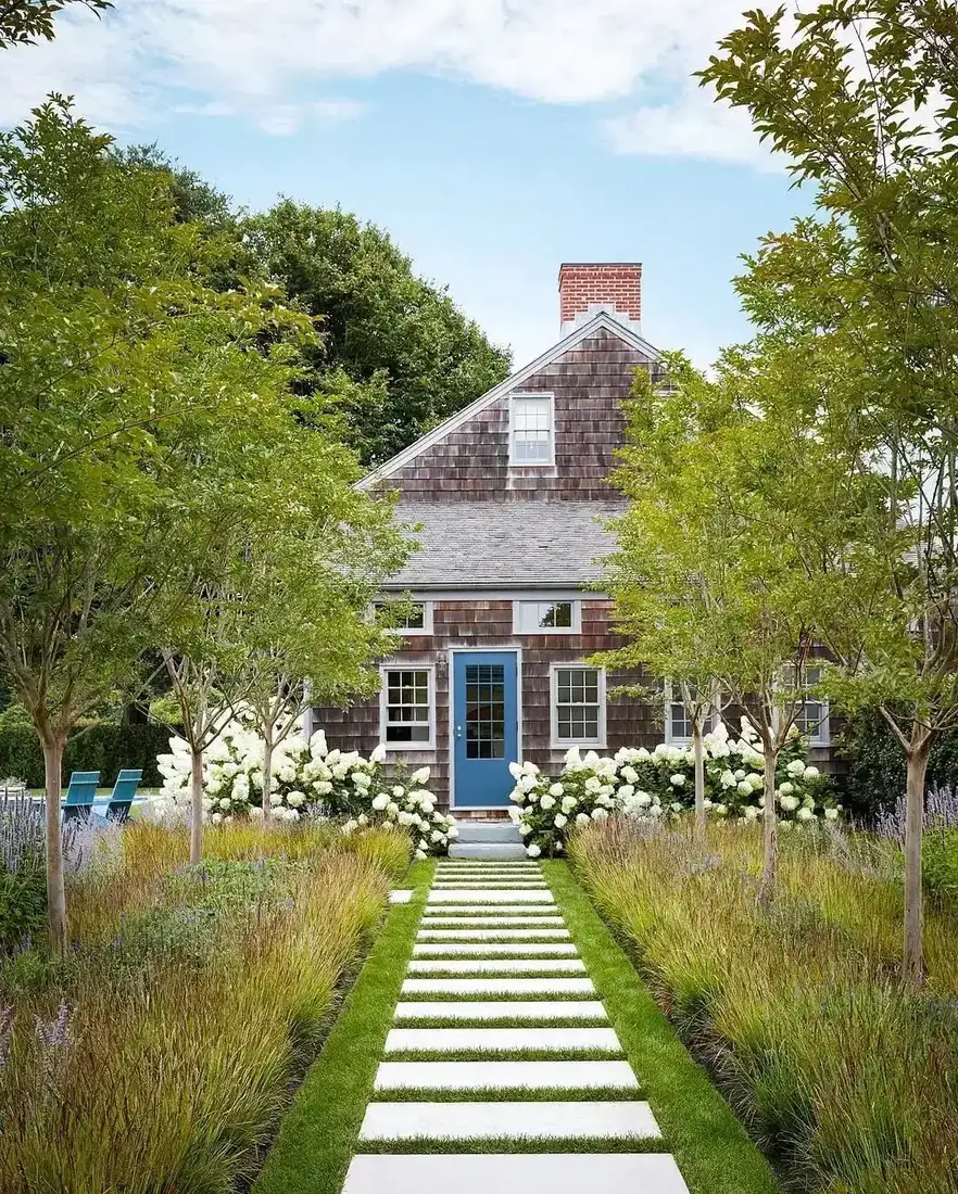 Shingle cottage with a dusty blue front door and a hydrangea lined walkway