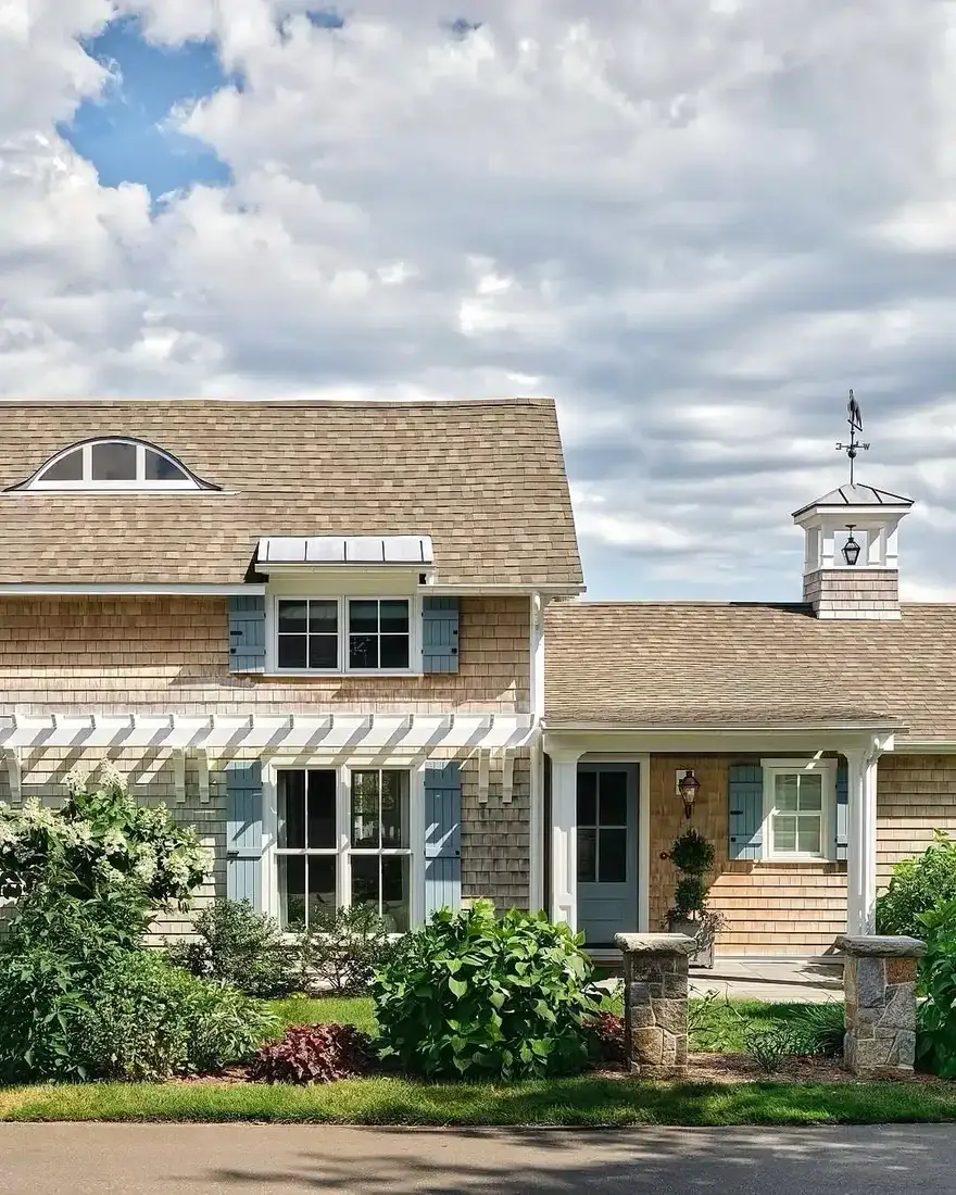 Shingle cottage with blue shutters and a white cupola on the roof
