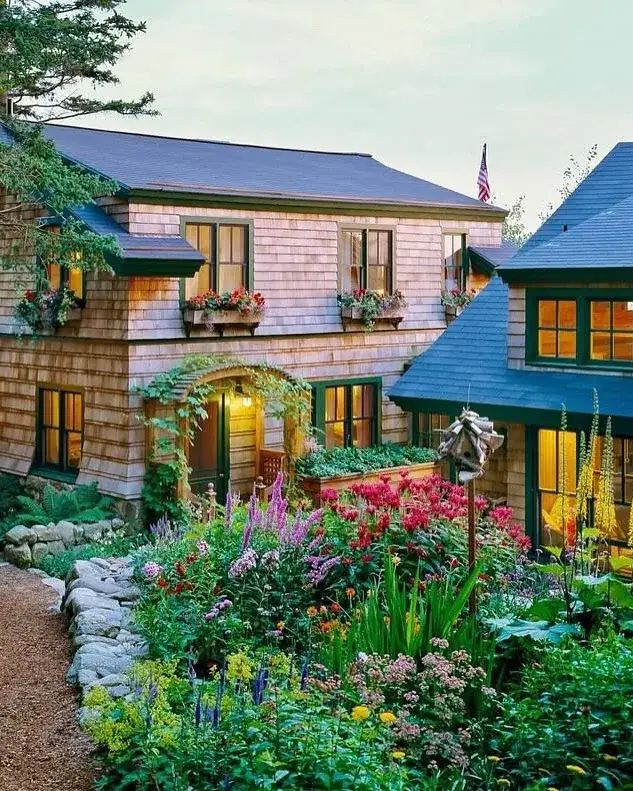 Shingle cottage nearly hidden among cottage garden flowers and lawn
