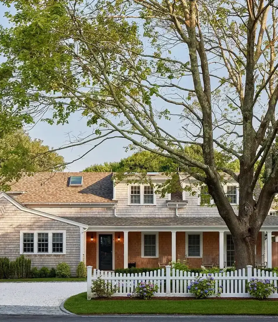 Shingle cottage with a white picket fence and hydrangeas along the front