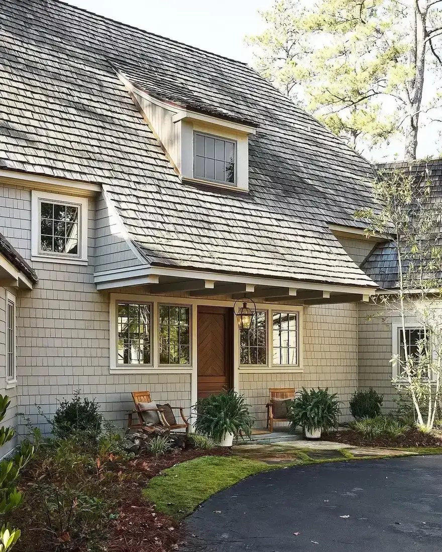 Shingle cottage with a warm wood door and a curved gravel driveway