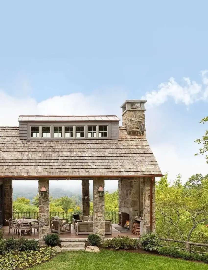 Shingle lodge with stone columns and an outdoor fireplace on the porch