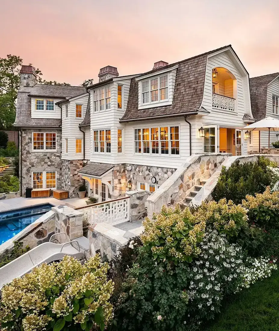 Shingle style mansion with a pale stone terrace and swimming pool