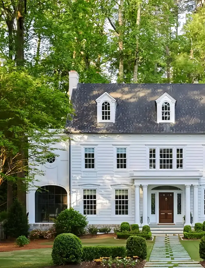 White clapboard colonial with a grey stone band under the cladding and a pale slab path between clipped box balls