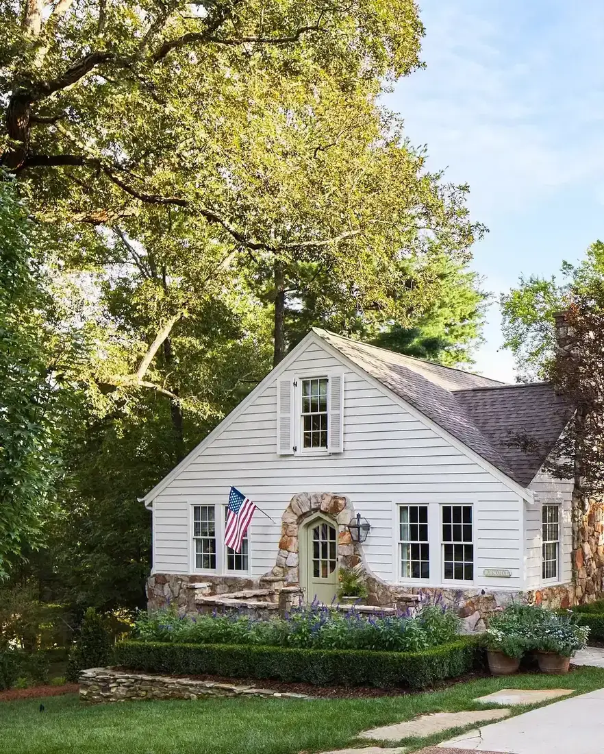 Small white clapboard cottage with a fieldstone skirt running up into a stone arch around the front door