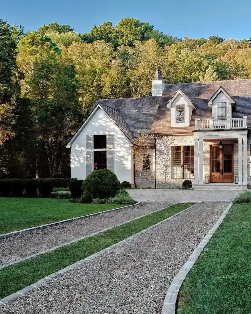 Gravel drive edged in pale stone leading to a house with a fieldstone entry bay running full height to the gable