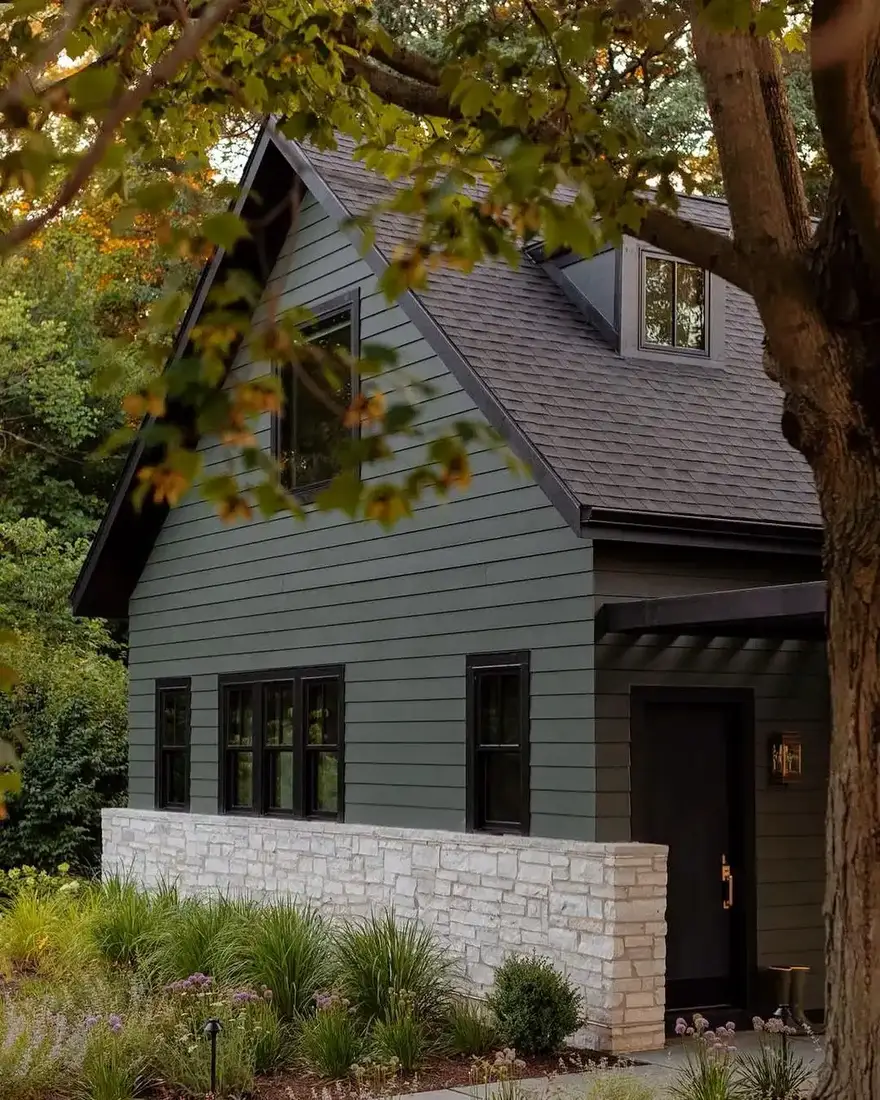 Dark green cottage with a pale stone base running to sill height under black framed windows