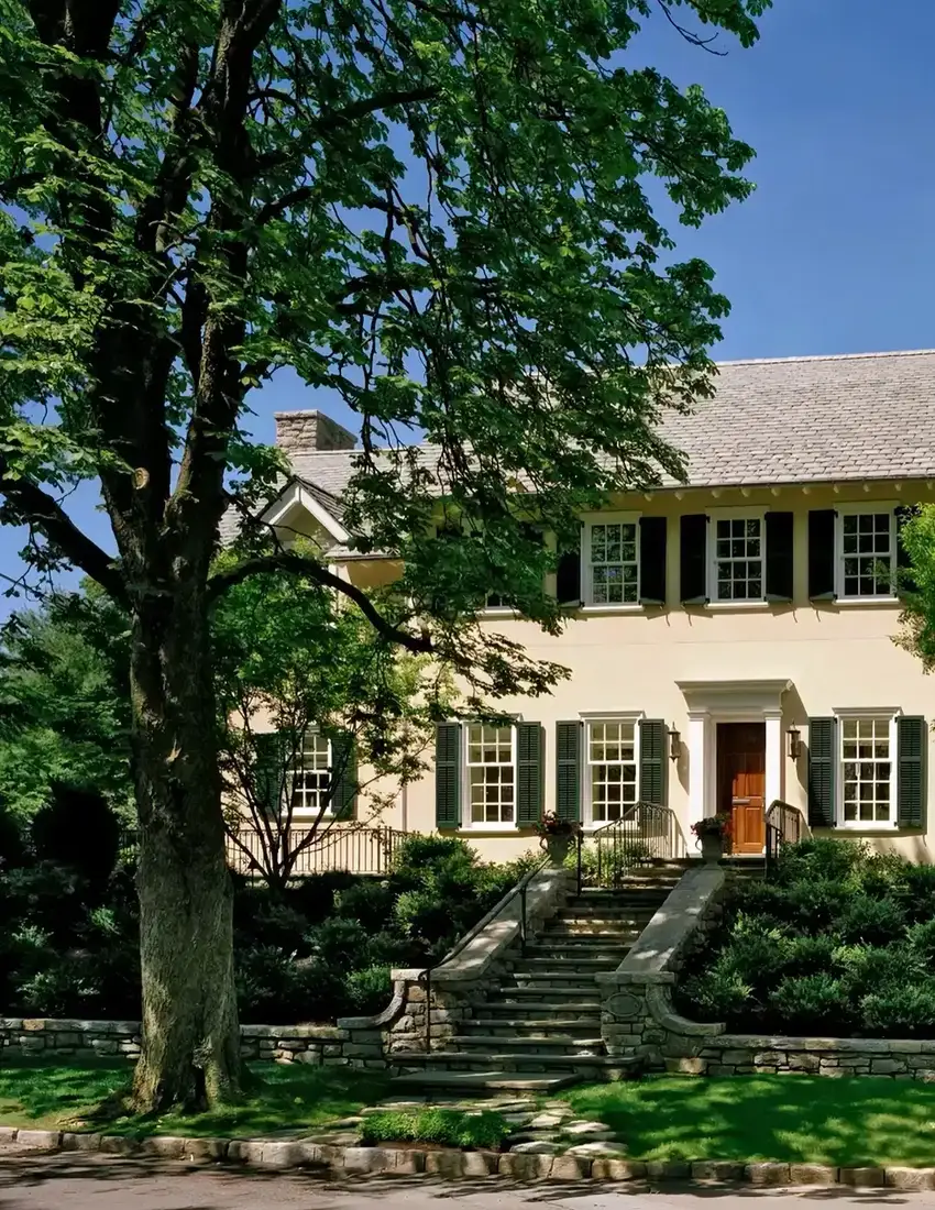 Cream colonial house with dark shutters above stone entrance steps and flanking stone cheek walls