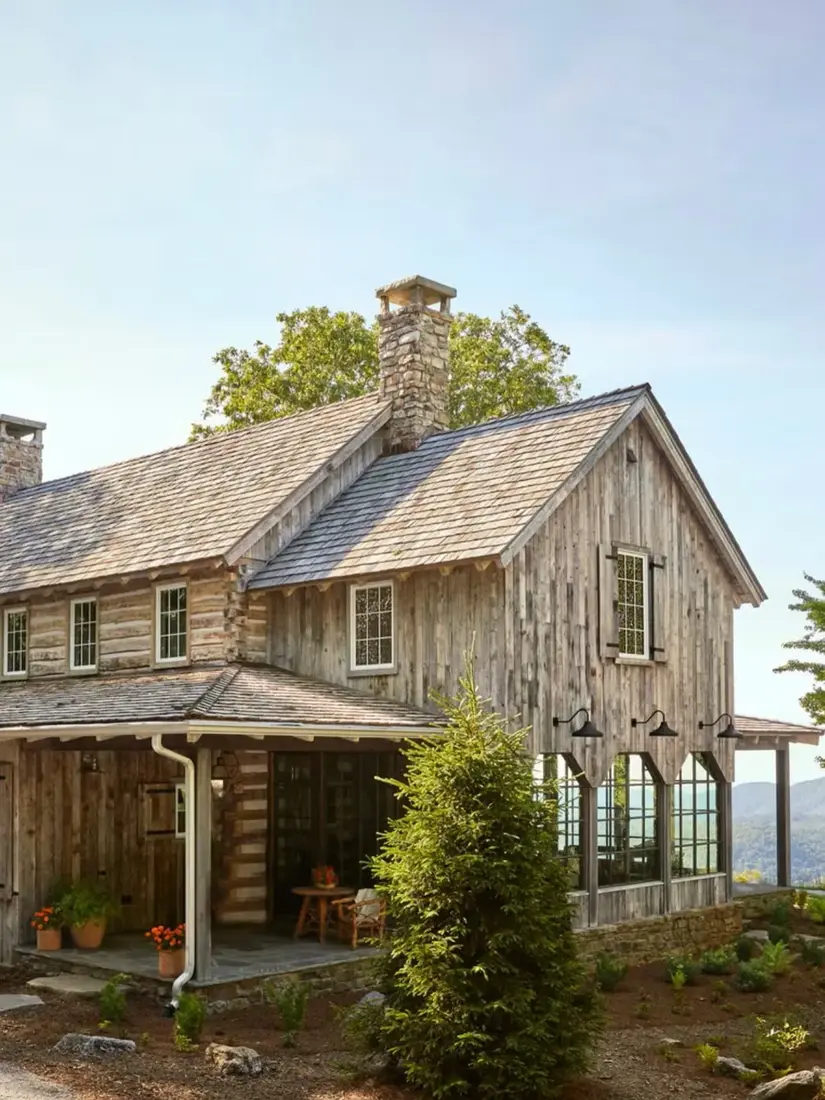 Weathered barnwood house with a tall fieldstone chimney and a stone plinth under the glazing