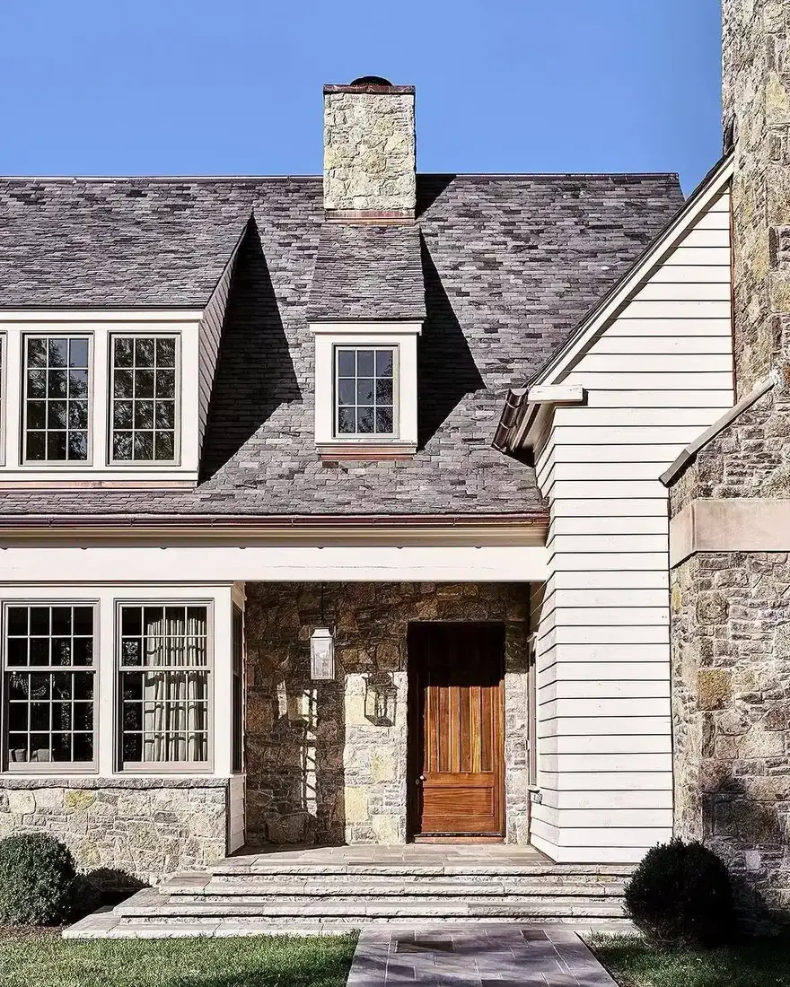 Stone ground floor porch bay with a timber door under white clapboard and a grey slate roof