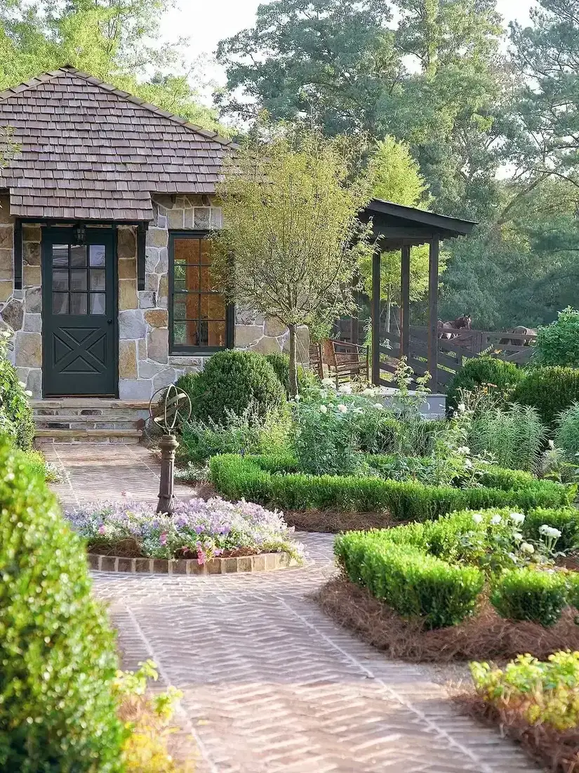 Full height rubble stone cottage with a dark ledged door, brick path, and clipped boxwood set forward of the wall